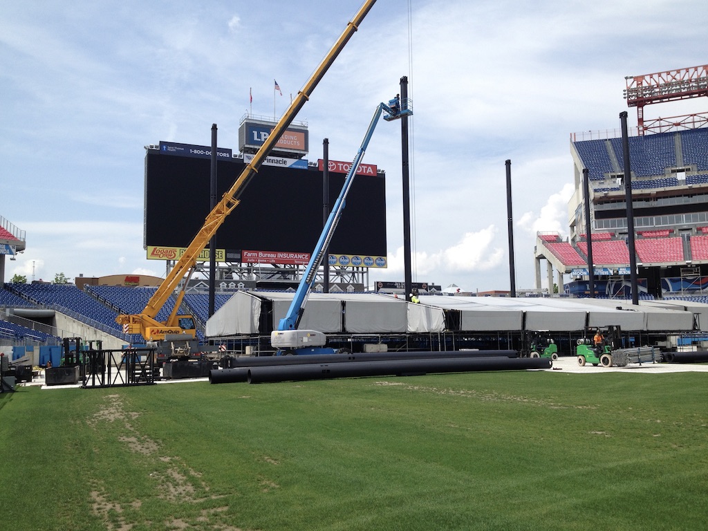 Early CMA Fest build at Nissan Stadium — grass field, cranes beginning stage construction